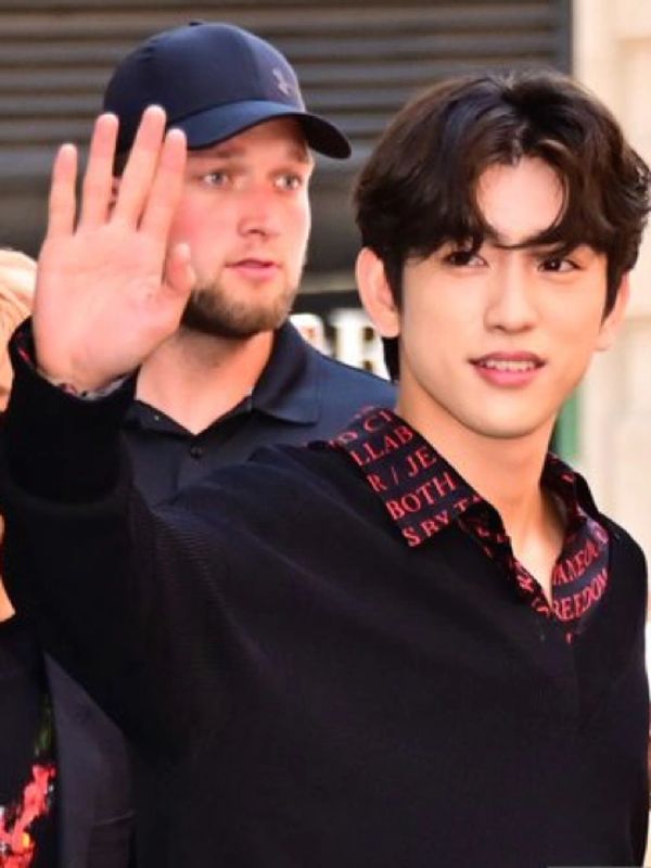 Young man waving, with a bearded man in background.