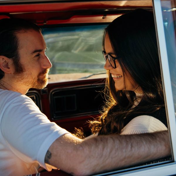 a man and a woman sit in a vintage red truck at golden hour, smiling at each other
