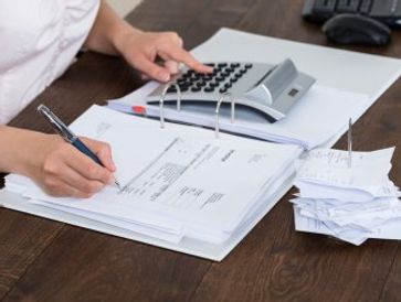 Person using a calculator and writing on documents at a desk.