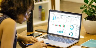 Woman analyzing financial charts on a laptop at a wooden table.