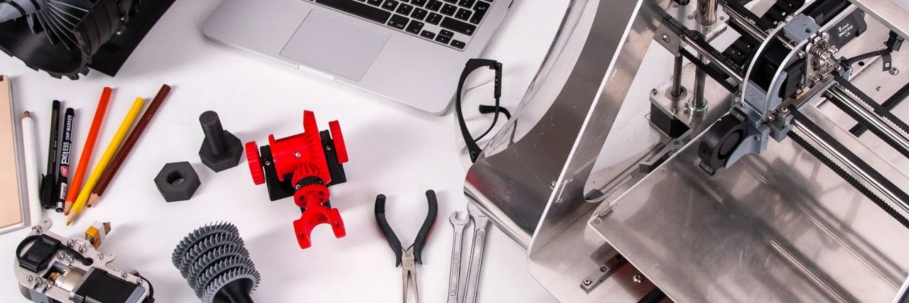 messy desk full of3D printed parts, tools, apple laptop and a 3D printer.