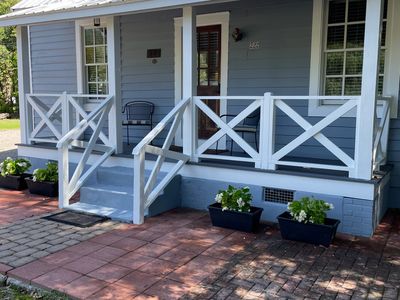 Cozy blue house porch with white railing and plants.