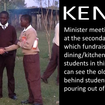 Minister meets school students in Kenya near old kitchen with smoke.