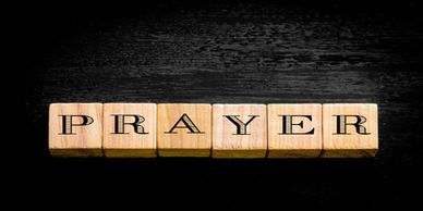 Wooden blocks spelling 'PRAYER' on black background.