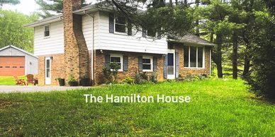 A two-story house named The Hamilton House surrounded by greenery.