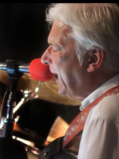Elderly man singing into a red microphone during a live performance.