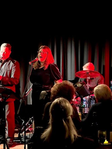 A band performs live on stage with a singer in red lighting.