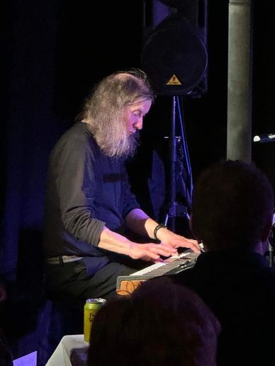 Man with long hair playing keyboard in a dimly lit room.