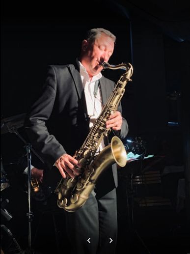 Man in suit passionately playing a saxophone on stage.