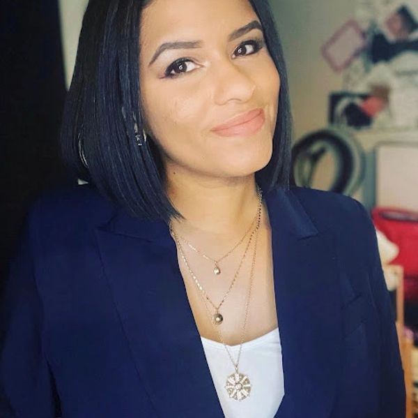 Woman with shoulder-length black hair wearing a navy blazer and layered necklaces.