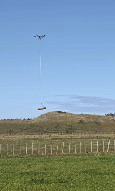 Drone lifting a log over a grassy hill.