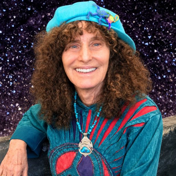 Woman with curly hair smiling, wearing a blue hat and colorful outfit.