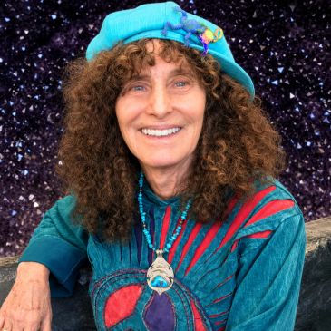 Woman with curly hair smiling, wearing a blue hat and colorful outfit.