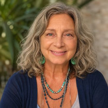 Smiling older woman with wavy gray hair outdoors.
