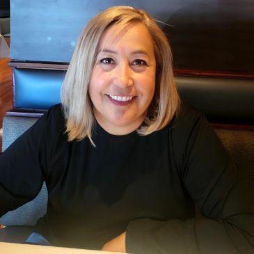 Smiling woman with blonde hair sitting in a restaurant booth.