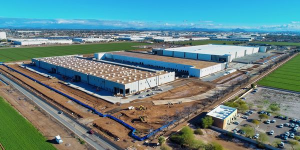 Aerial view of a large industrial warehouse under construction surrounded by green fields.