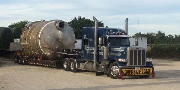Blue semi truck hauling an oversized industrial tank on a flatbed trailer.