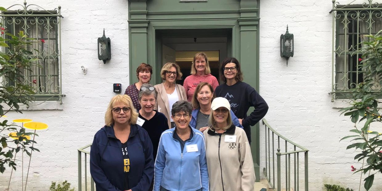 Group of nine smiling women standing in front of a green entrance.