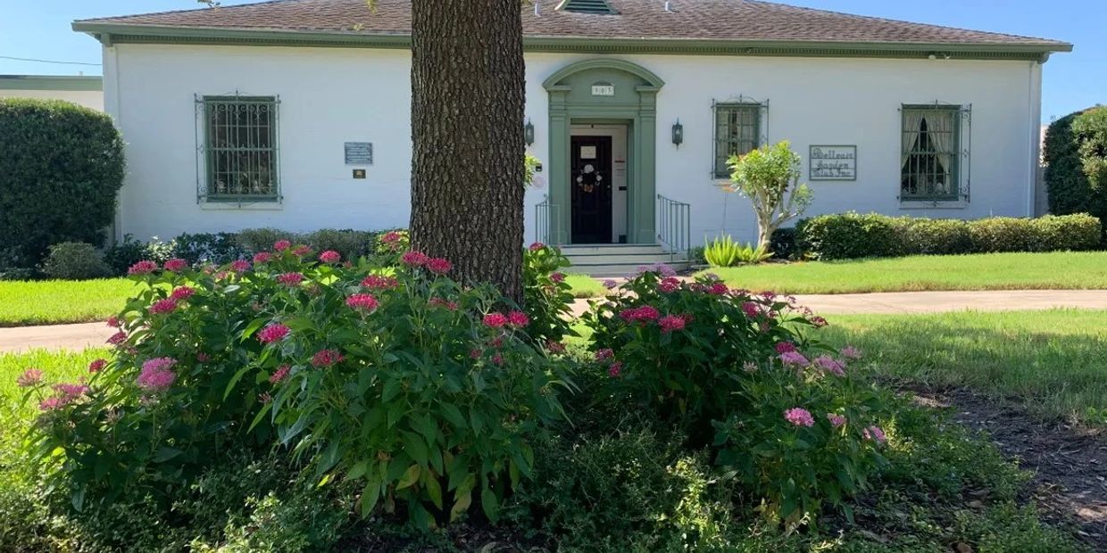 White building with green trim and flower bushes in front.