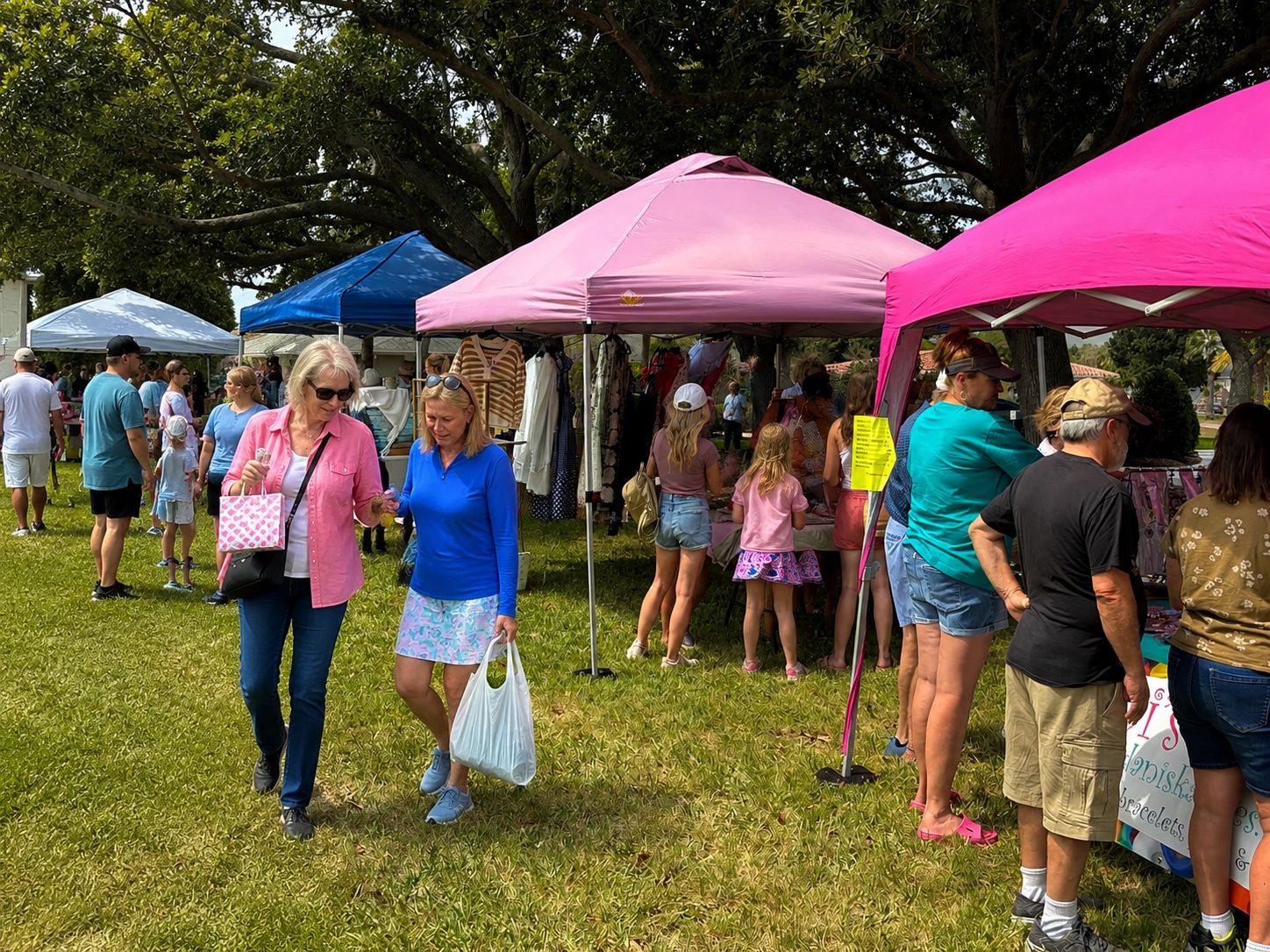 People shopping and socializing at an outdoor market with colorful tents.