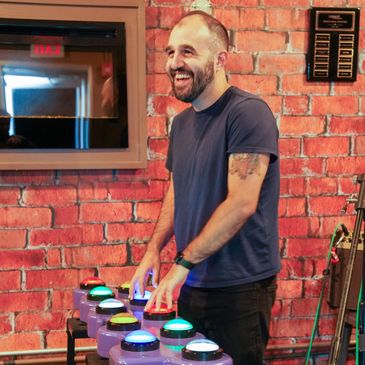 Man smiling while pressing colorful buttons against a brick wall.