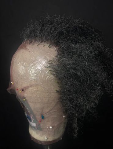 Curly gray wig styled on a mannequin head with pins and netting.