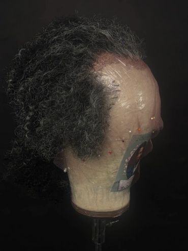 Side view of a wig on a mannequin head against a dark background.
