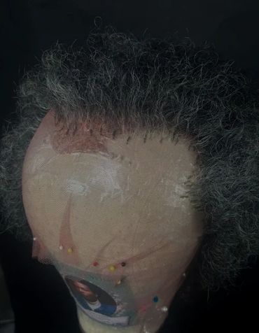 A wig cap with gray curly hair and pins attached to it.