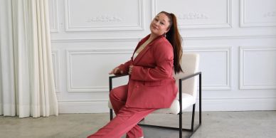Femme souriante en tailleur rouge assise sur une chaise.