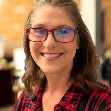Smiling woman wearing red glasses and a red plaid shirt.