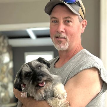 Man in a cap holding a happy dog indoors.