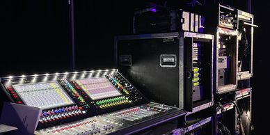 Audio mixing console and equipment racks in a dark room.