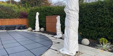 Backyard pool covered with protective tarps and wrapped Niagara Tropics cold hardy palm trees for winter.