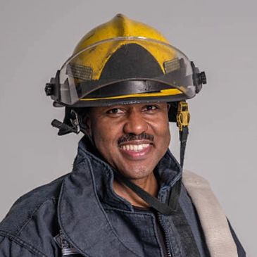 Smiling firefighter in yellow helmet and protective gear.