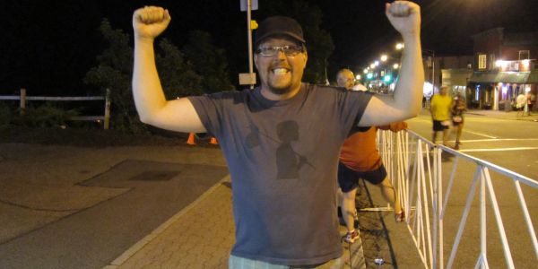 Homme souriant levant les bras en l'air la nuit.