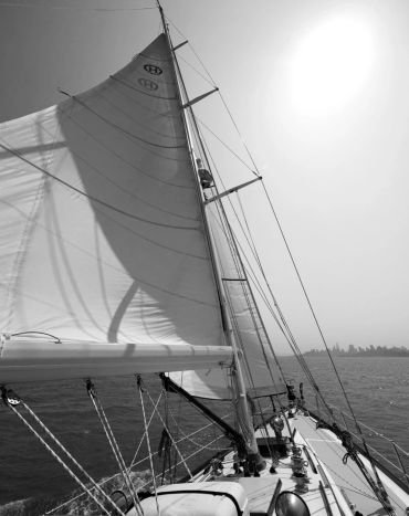 Black and white photo of a sailboat with its sail up on a sunny day.