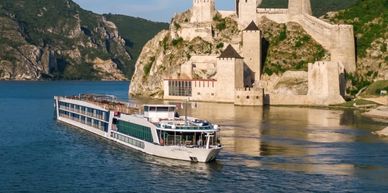 A river cruise ship sails past an ancient stone fortress on a sunny day.