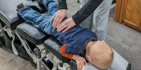 Little boy face down on a chiropractic table while the chiropractor evaluates his spine. 