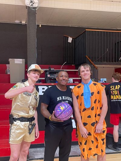 Three people posing in a gym, one in gold costume, one holding basketball, one in Fred Flintstone costume.