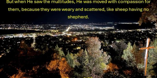 City lights at night with a wooden cross and scripture text.