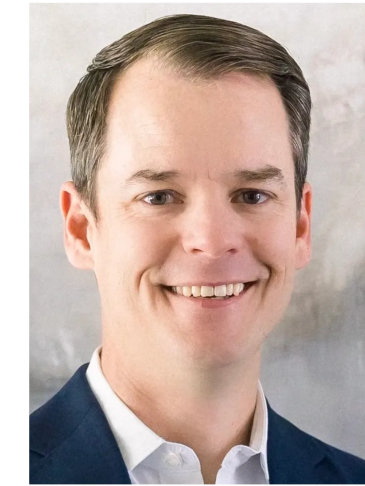 Smiling man in a suit with a light background.