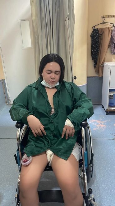 Person resting in a wheelchair wearing a green jacket and a mask below the chin.