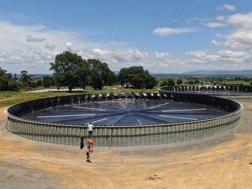 Two people walking near a large circular water treatment tank outdoors.