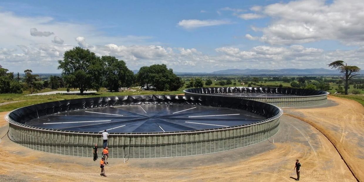 Two large circular water tanks with people around them in a rural setting.