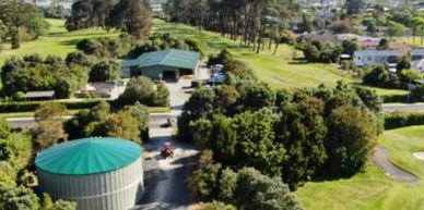 Aerial view of a green-roofed building and water tank surrounded by trees and grass.