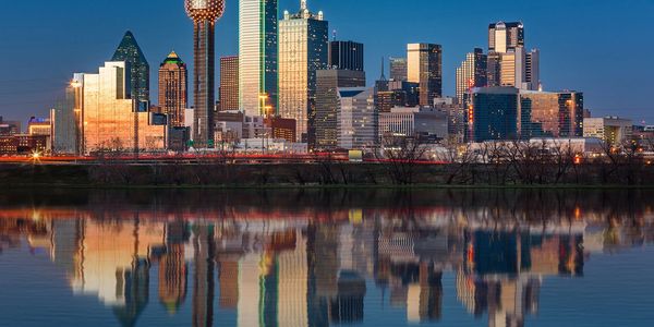 Dallas city skyline reflected in calm water during sunset.
