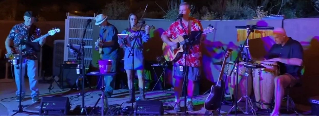 A band performs live outdoors at night with various instruments and colorful lighting.