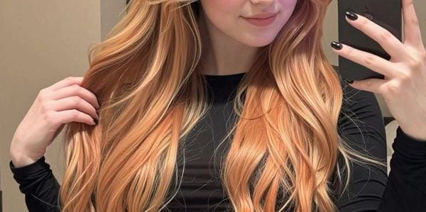 Young woman with long, wavy blonde hair taking a mirror selfie.