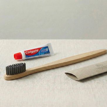 Eco-friendly bamboo toothbrush with Colgate toothpaste tube and paper packaging.