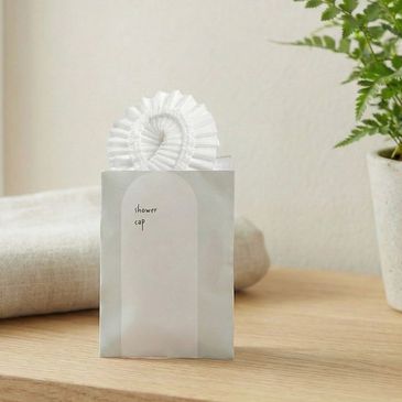 White shower cap in a minimalistic packaging on a wooden surface.